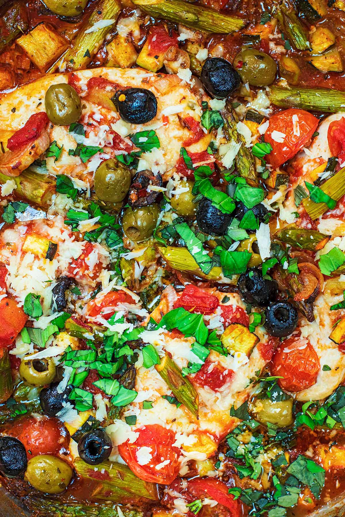 Cooked chicken breasts covered in olives and vegetables in a tomato sauce.