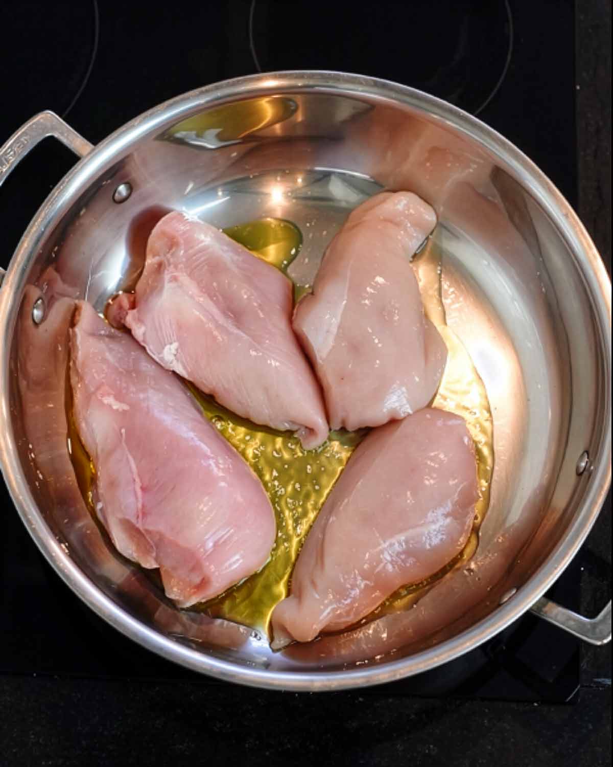 Four uncooked chicken breasts in a large silver pan.
