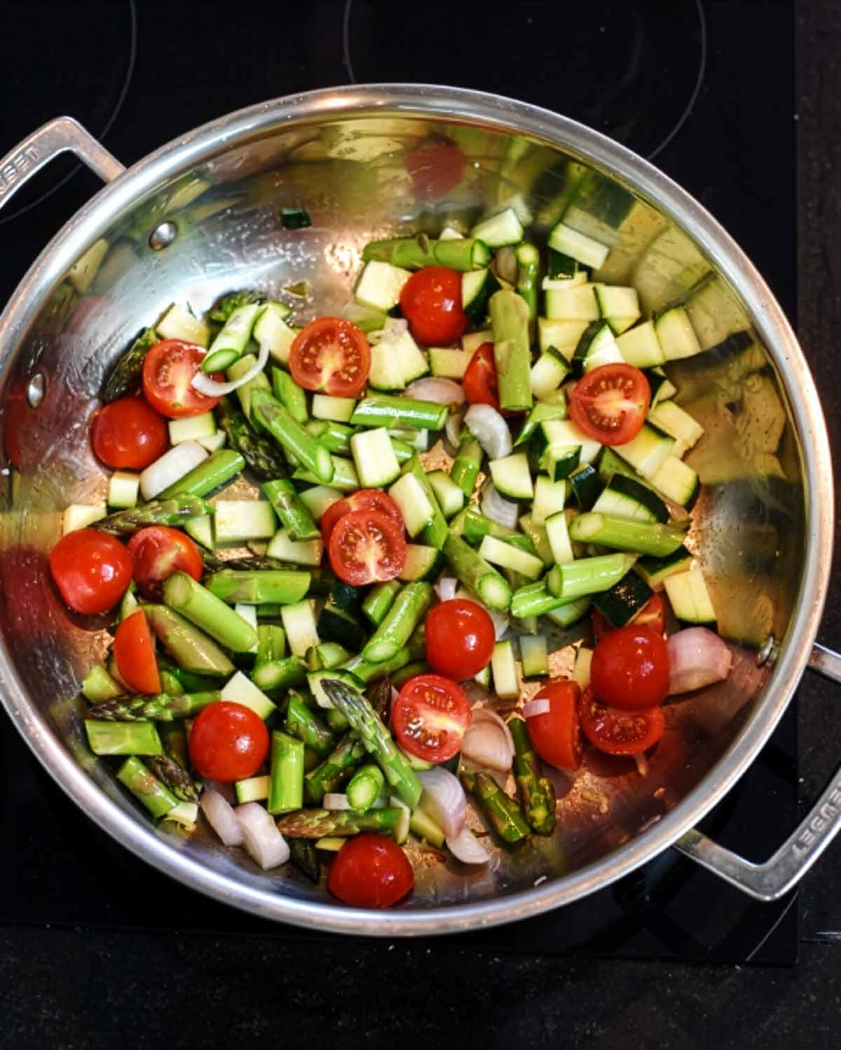 Chopped vegetables cooking in a large silver pan.