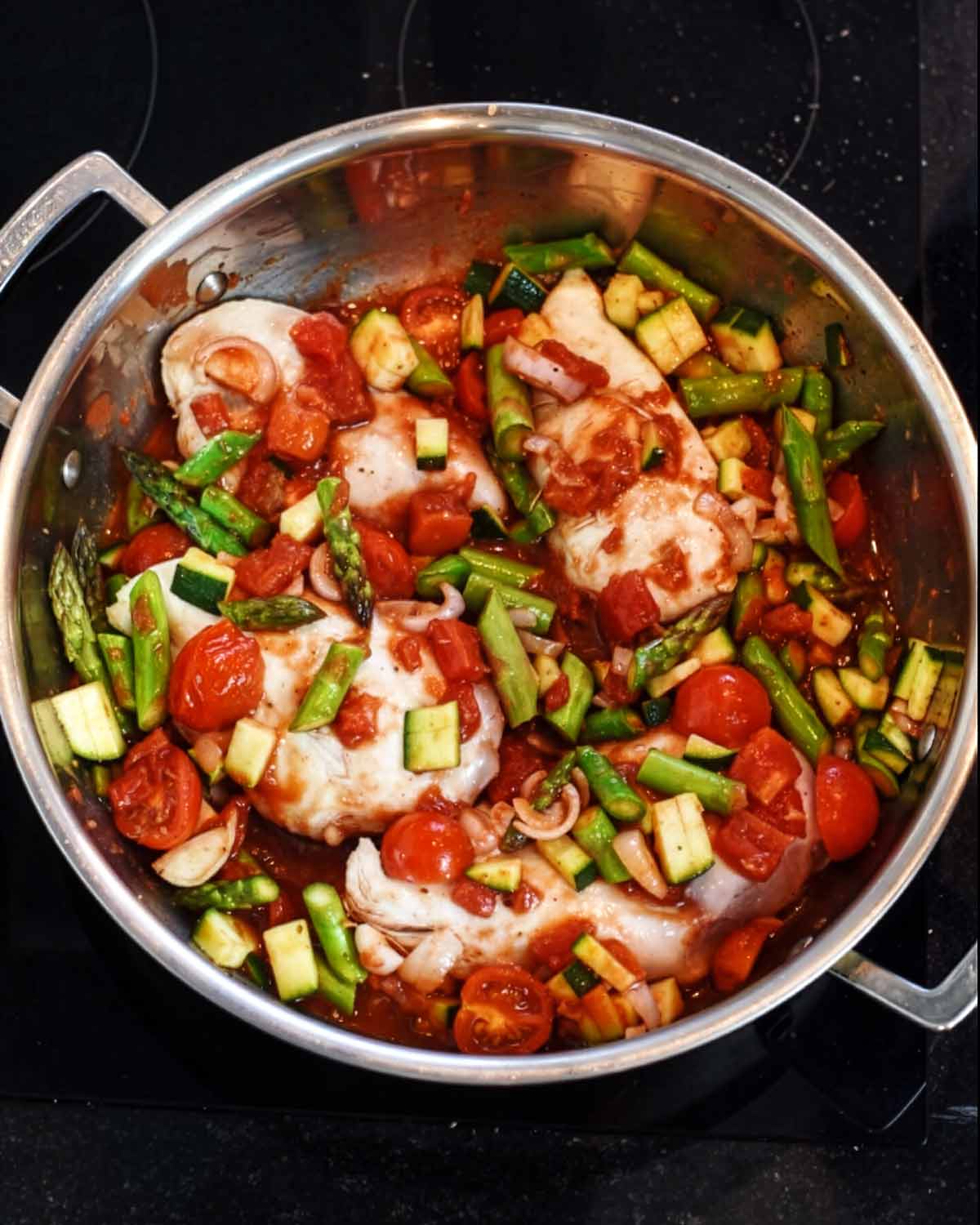 Chicken breasts and chopped vegetables in a large silver pan.