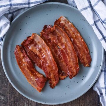 A plate of oven cooked bacon on a wooden surface.