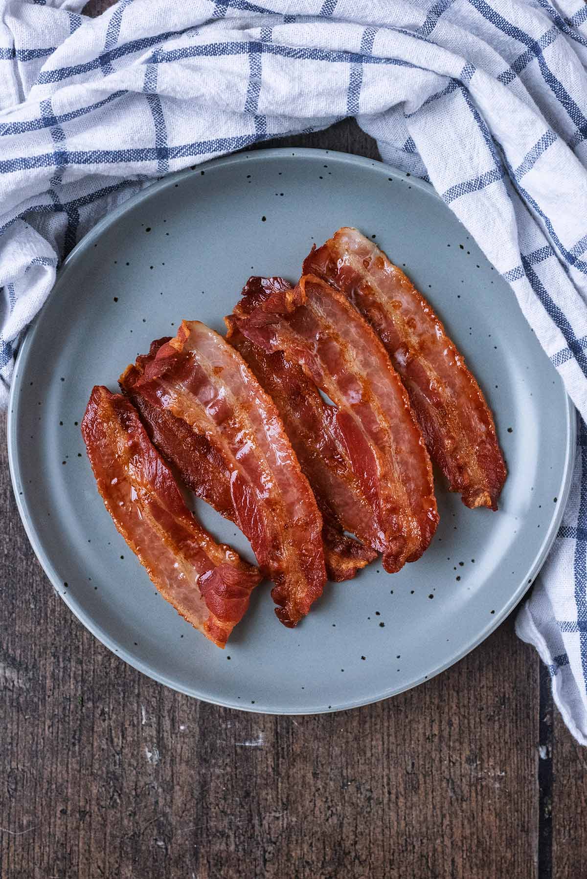 A plate of cooked bacon next to a checked towel.