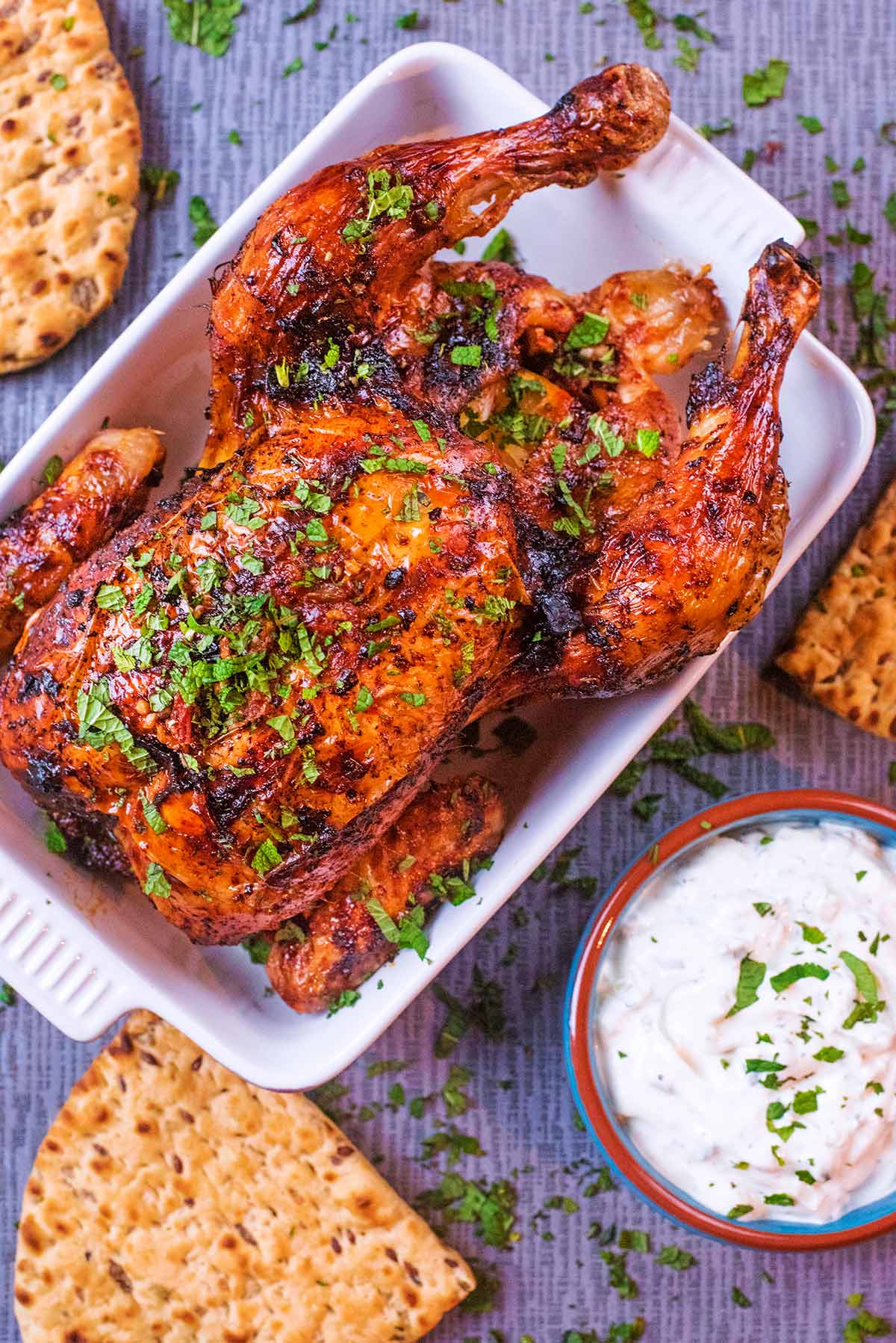 A whole roasted chicken in a baking dish next to flatbreads and dip.