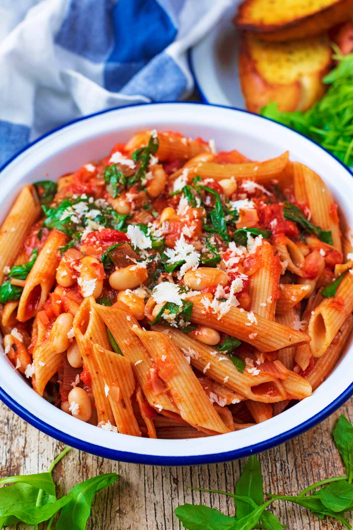 A bowl of pasta in a tomato sauce with beans and herbs.