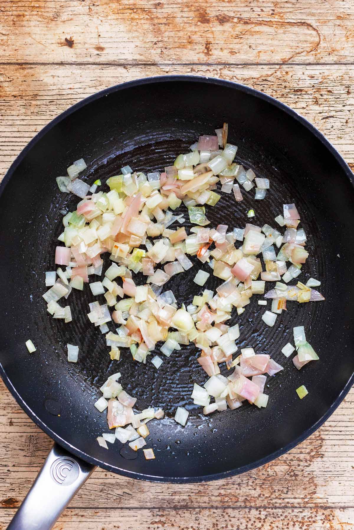 A frying pan with diced shallots in it.