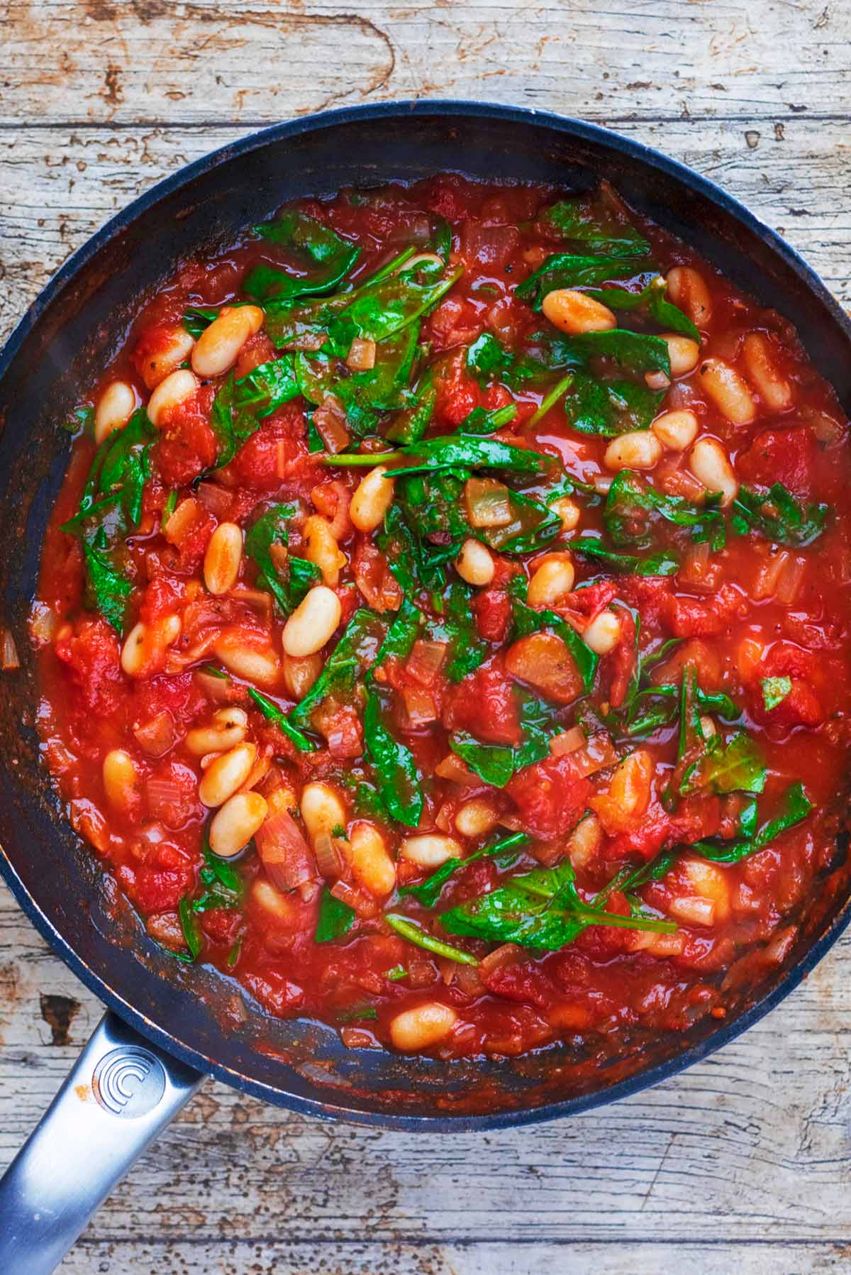 Pasta and beans in a frying pan in a tomato sauce with spinach.