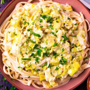 Creamy Leek Pasta in a pink bowl topped with chopped herbs.