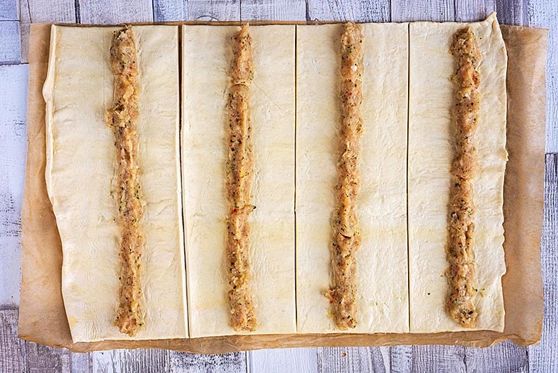 strips of pastry with sausage meat laying down the centre of them
