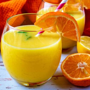 Two glasses of Immune Booster Juice next to orange and lemon halves.