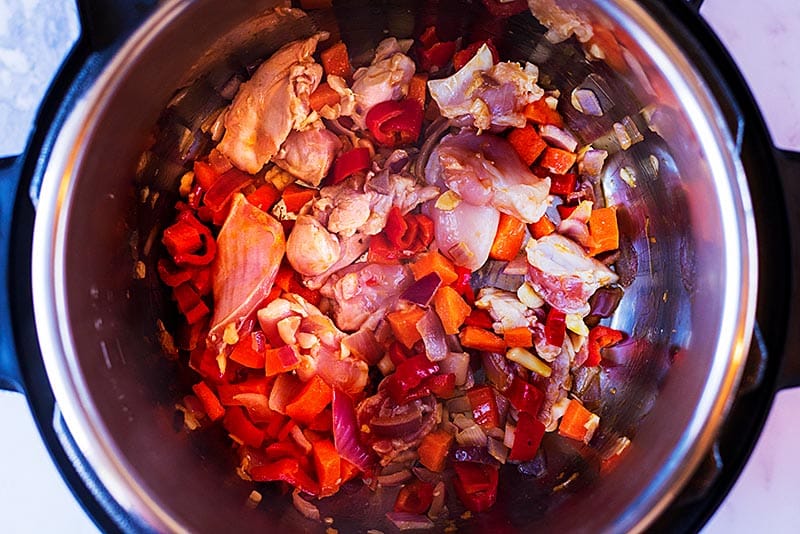 An instant pot with chopped vegetables and chunks of chicken.