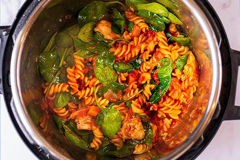 An instant pot bowl with tomato pasta and spinach.