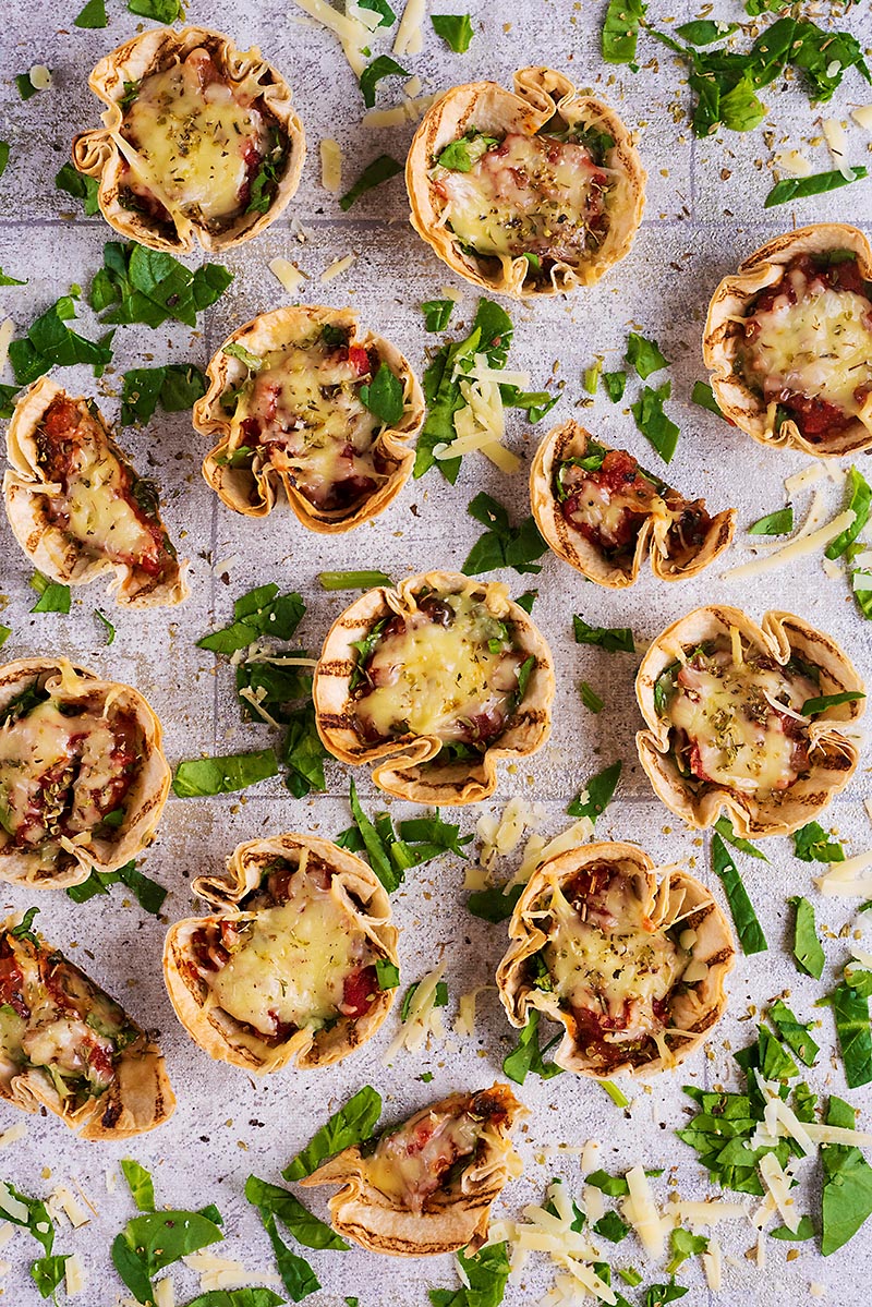Mini tortilla cup pizzas spread out over a tiled surface.