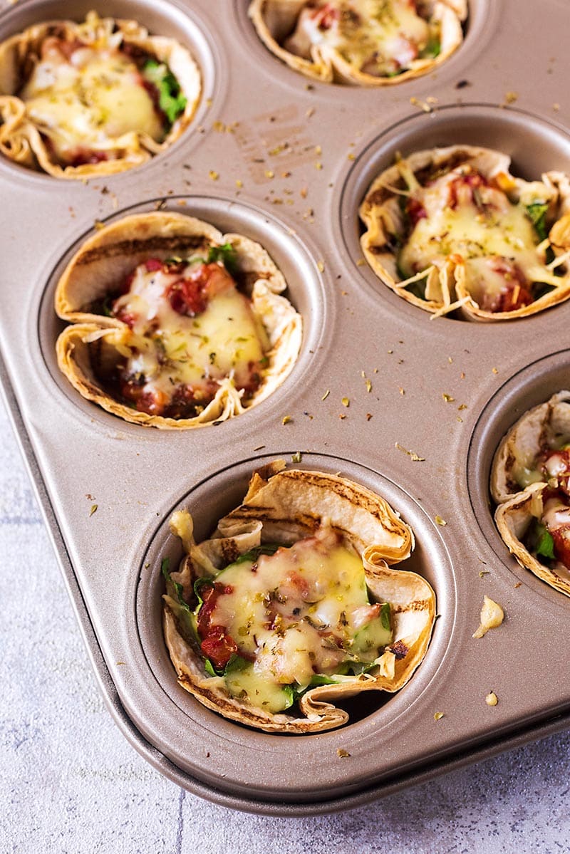 Cooked tortilla cups in a muffin tin.