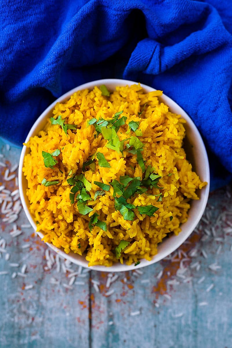 A bowl of yellow turmeric rice next to a blue towel.