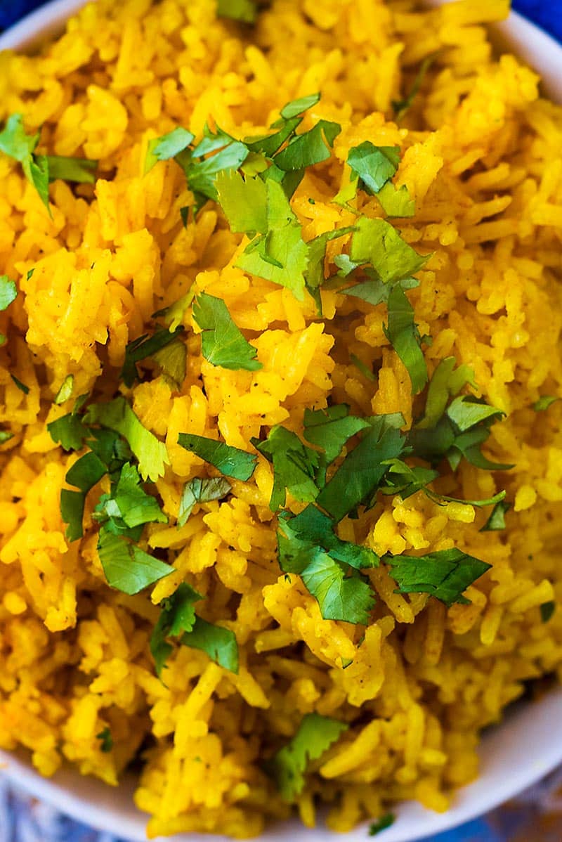Chopped green herbs on top of bright yellow rice.