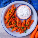 A plate of baked carrot fries with a small dish of dip.