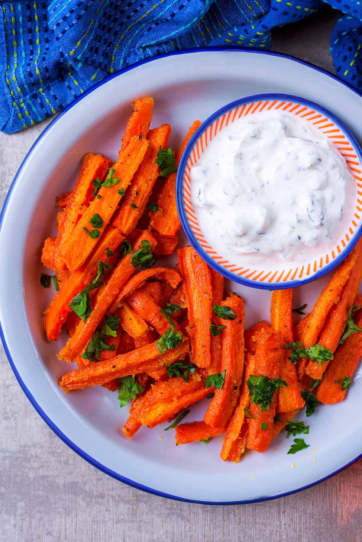 Carrot fries on a white plate with a dish of creamy white dip.