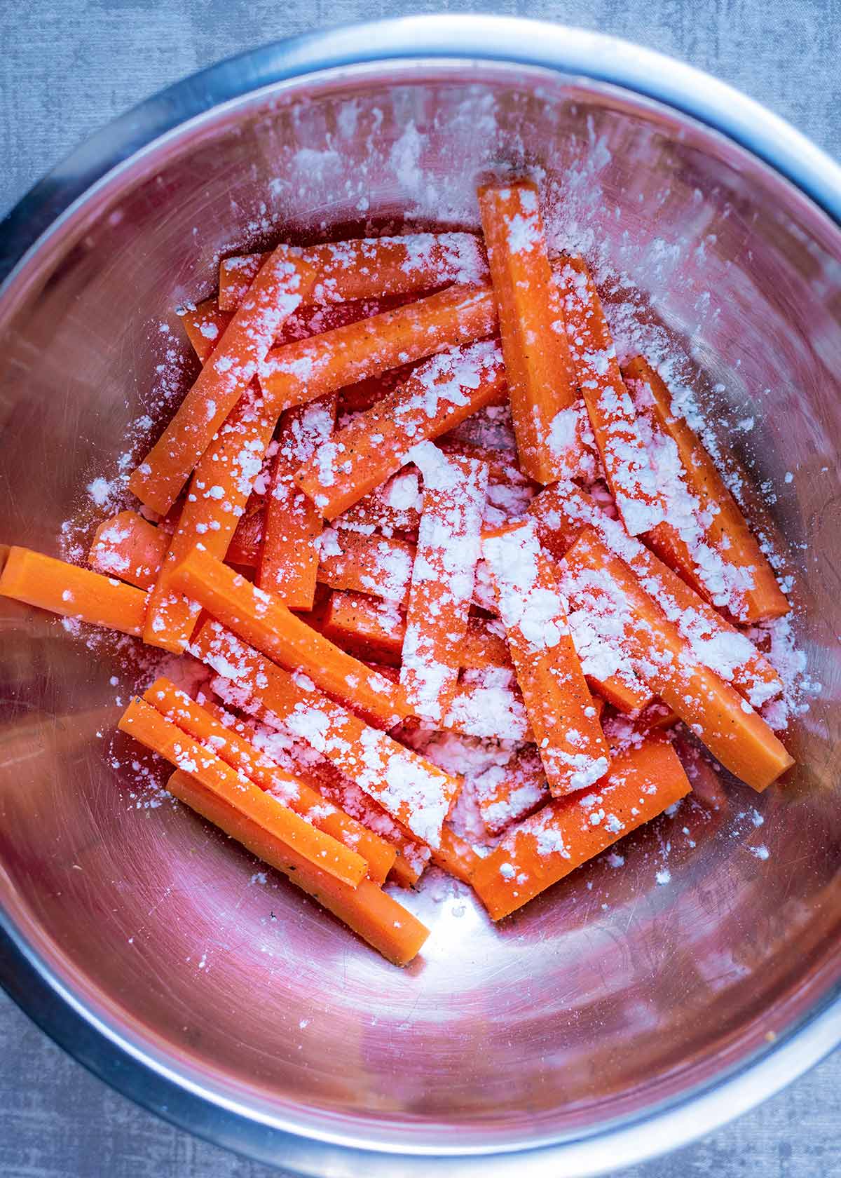 A large bowl full of carrot batons coated in cornflour.