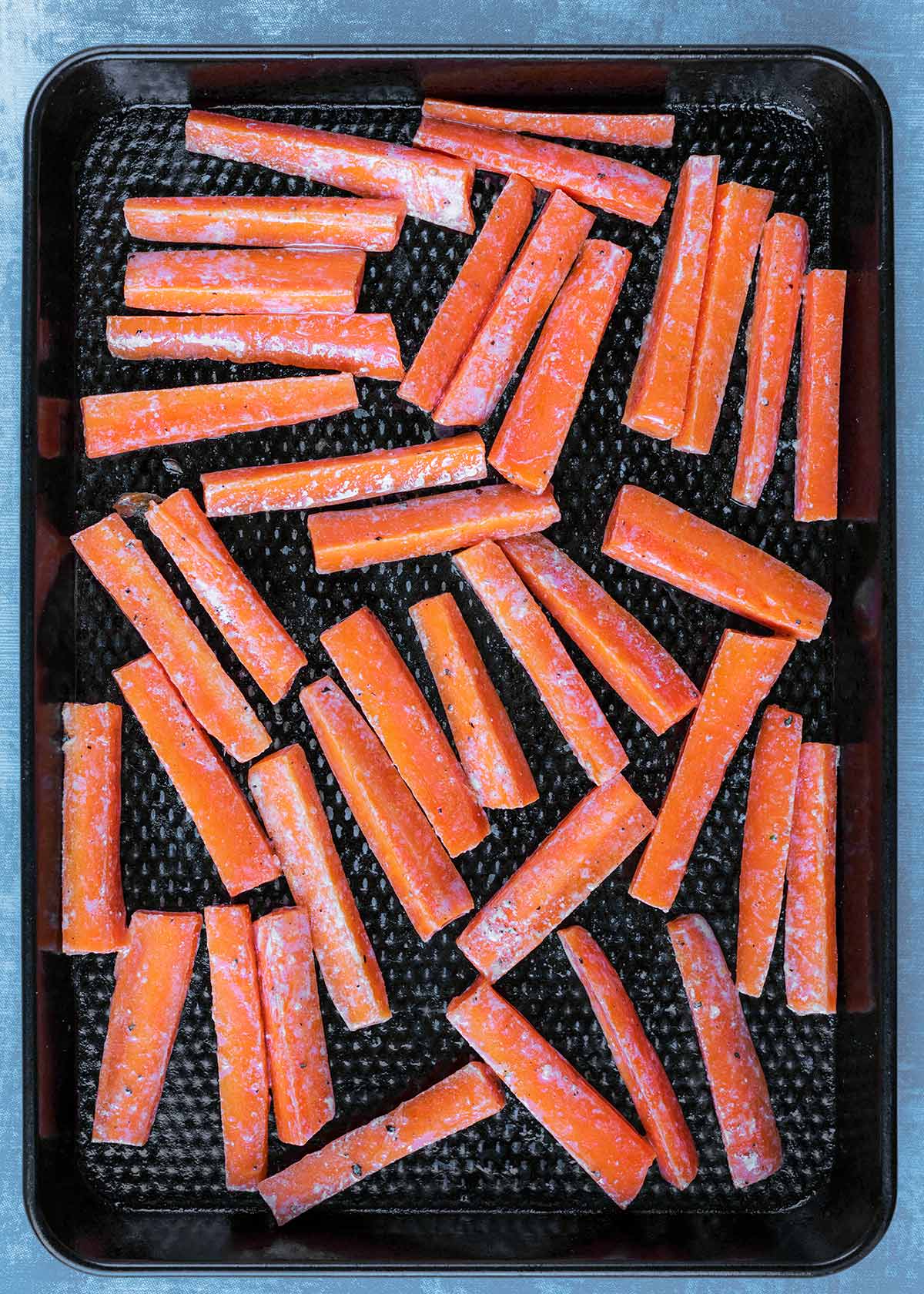 Carrot batons laid out on a black baking tray.