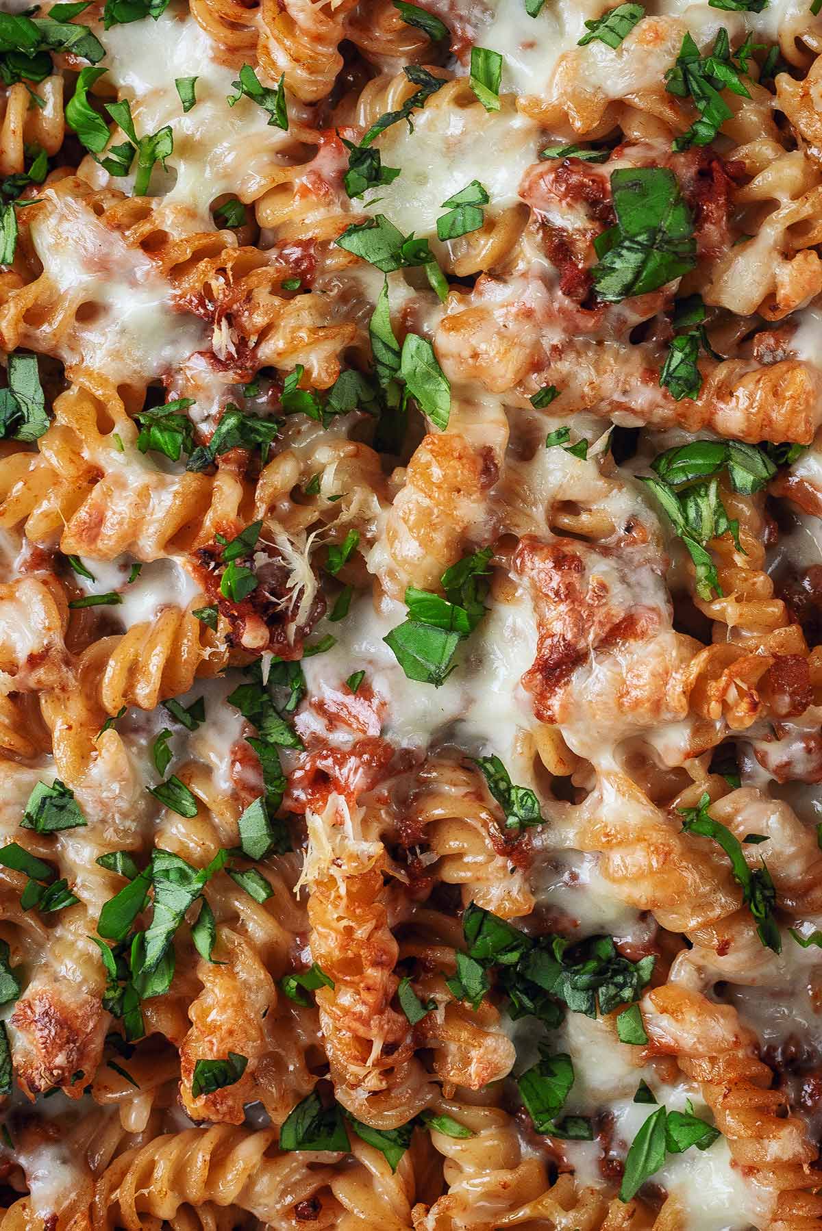 Melted cheese and chopped herbs covering a pasta bake.