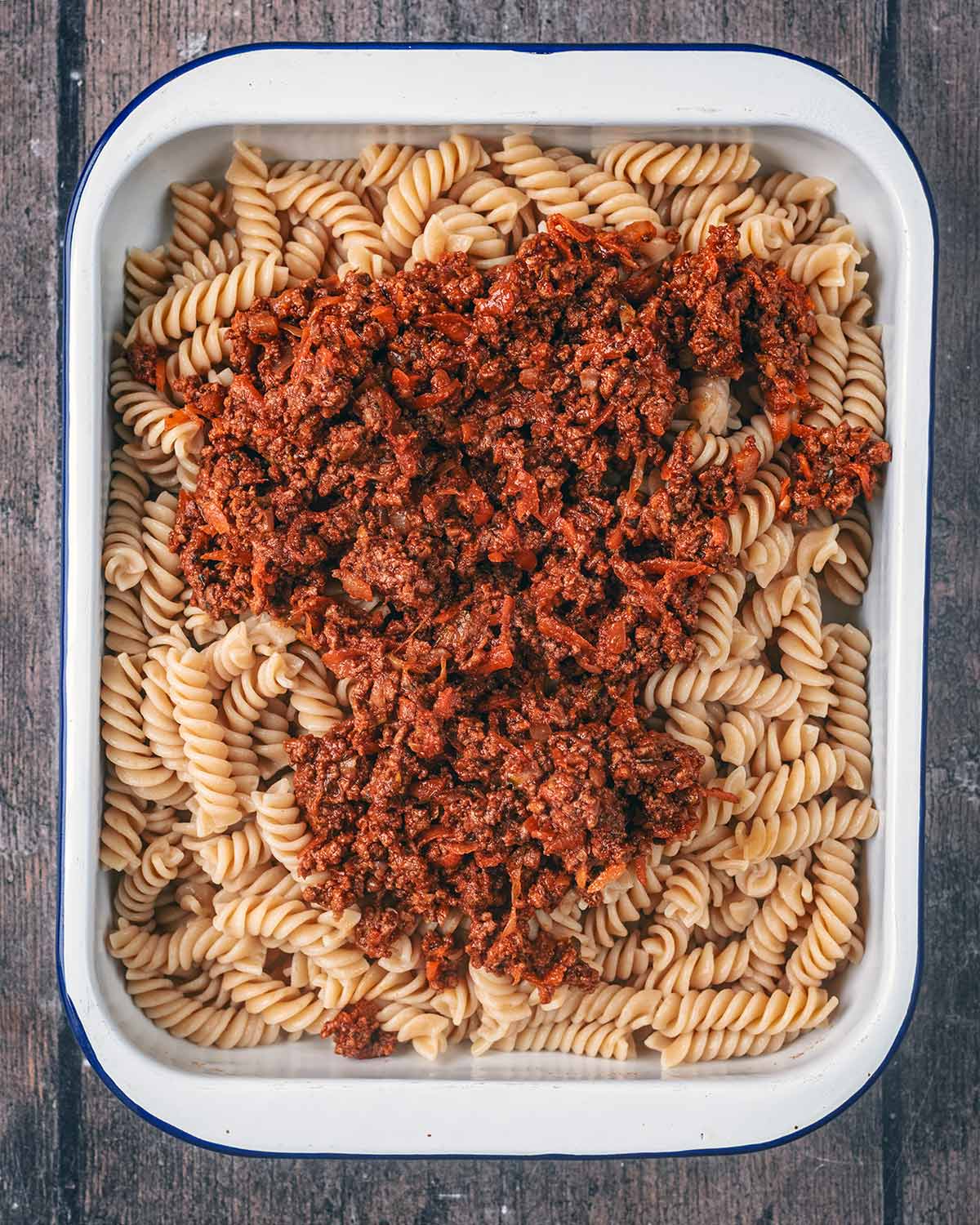Leftover bolognese on top of cooked pasta in a baking tray.
