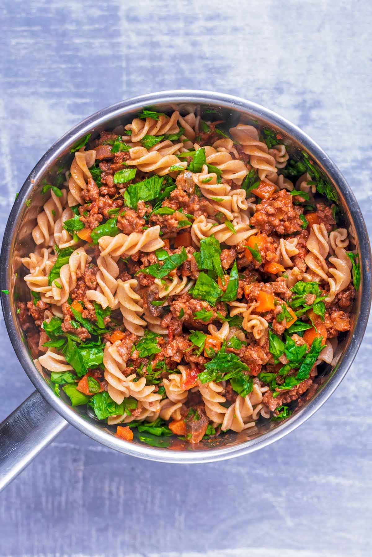 A saucepan full of pasta, bolognese and chopped basil.