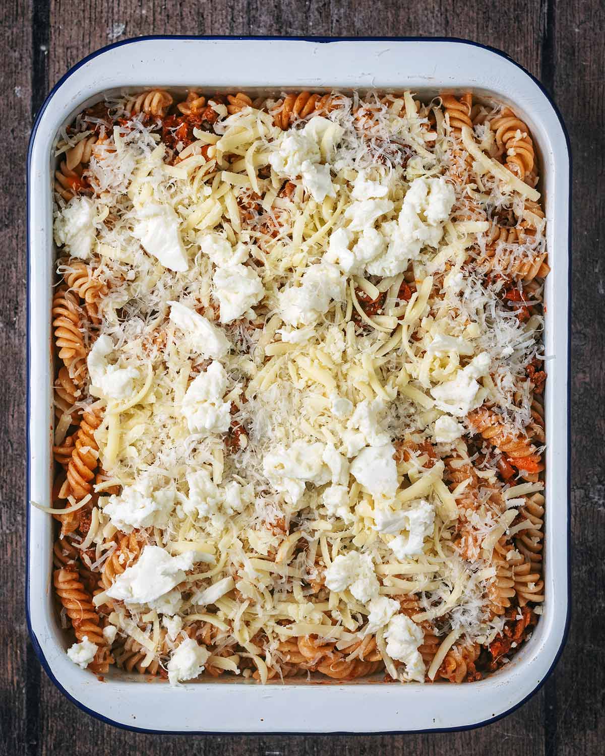 Pasta bolognese in a baking dish covered in grated cheese.