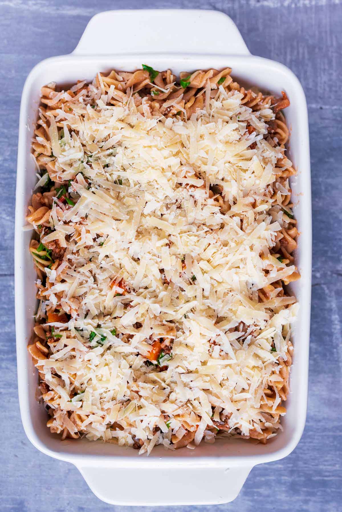 Pasta bolognese in a baking dish covered in grated cheese.