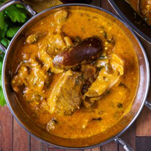 A bowl of creamy Lamb Korma next to a bunch of coriander, ginger, limes and aubergine.