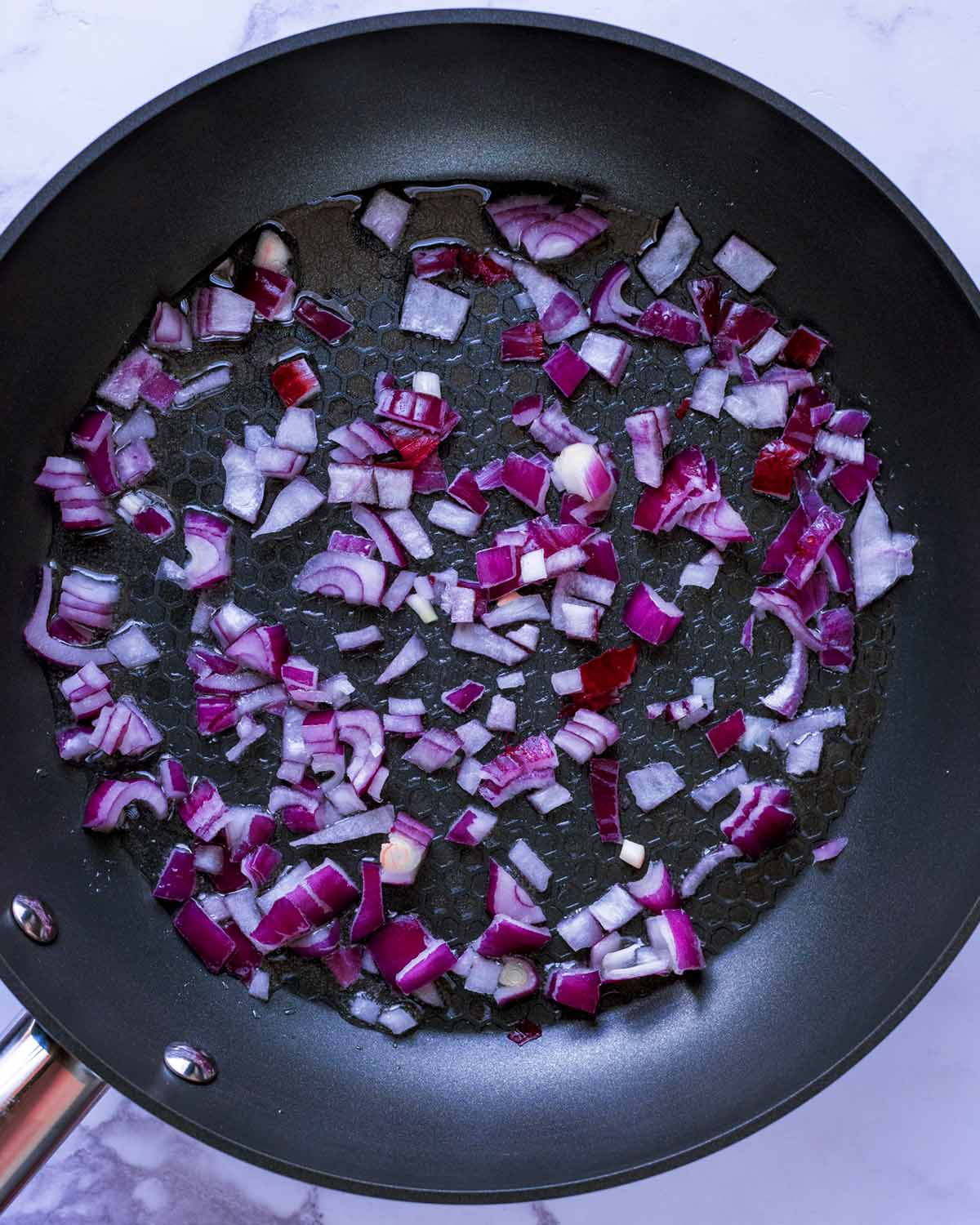 Chopped red onion cooking in a frying pan.