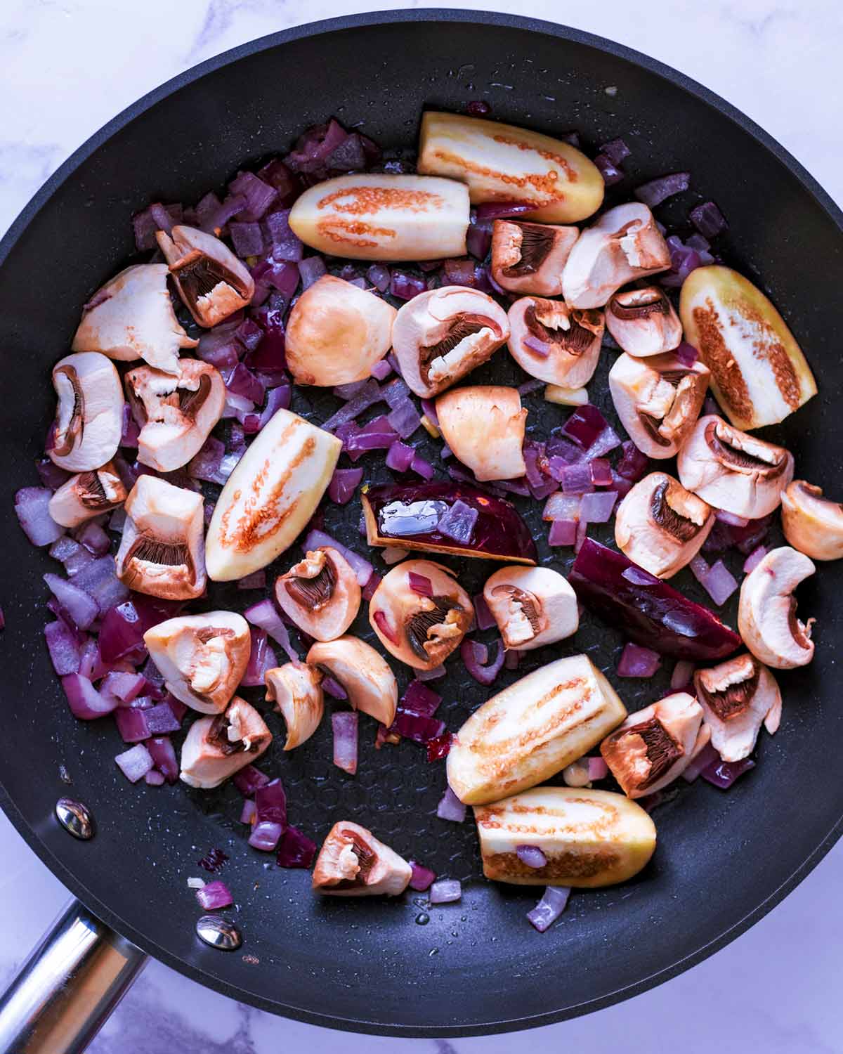 Red onion, chopped mushrooms and baby aubergines cooking in a pan.