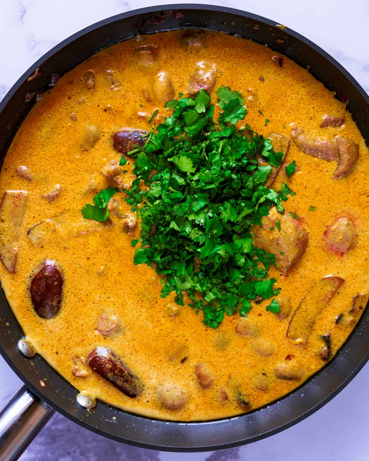 A yellow curry cooking in a pan with a large heap of chopped coriander in it.