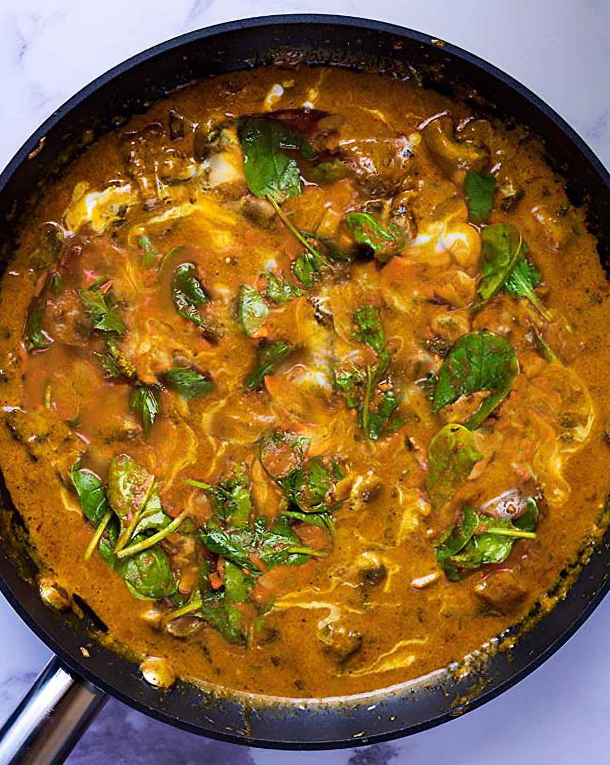 Lamb Korma in a pan with wilted spinach in it.
