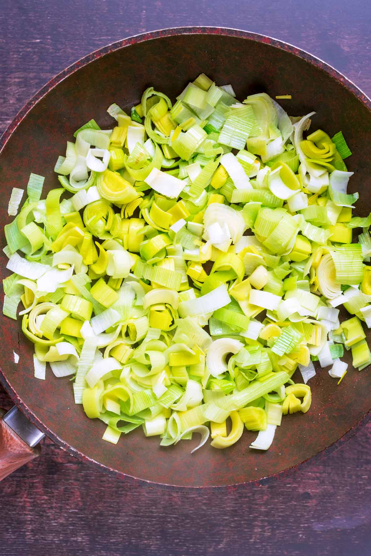 A frying pan with leeks cooking in it.