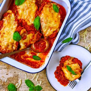 A plate of Healthy Eggplant Parmesan next to a baking tray with more of it in.