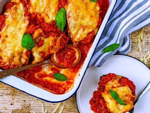 A plate of Healthy Eggplant Parmesan next to a baking tray with more of it in.