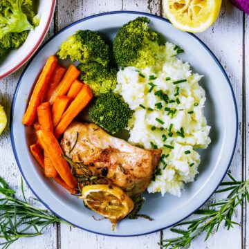 Lemon Rosemary Chicken thigh on a plate with mashed potato, carrots and broccoli.