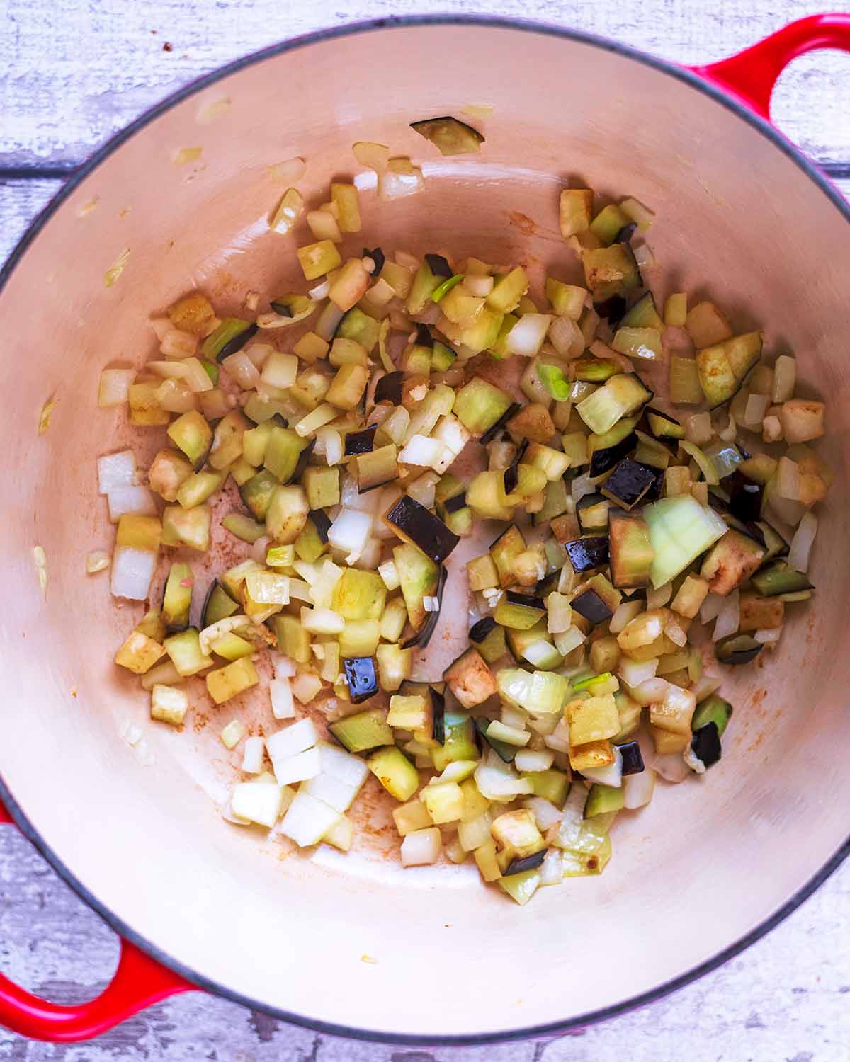 A large pan with shallots, garlic and eggplant cooking in it.