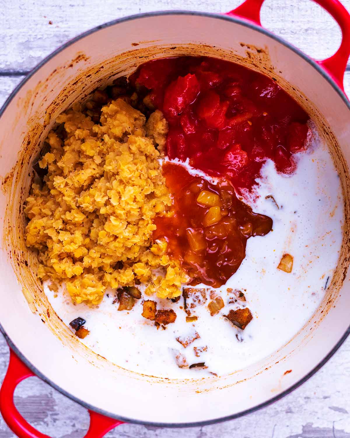 Chopped tomatoes, vegetables, coconut milk and cooked lentils cooking in a large pan.