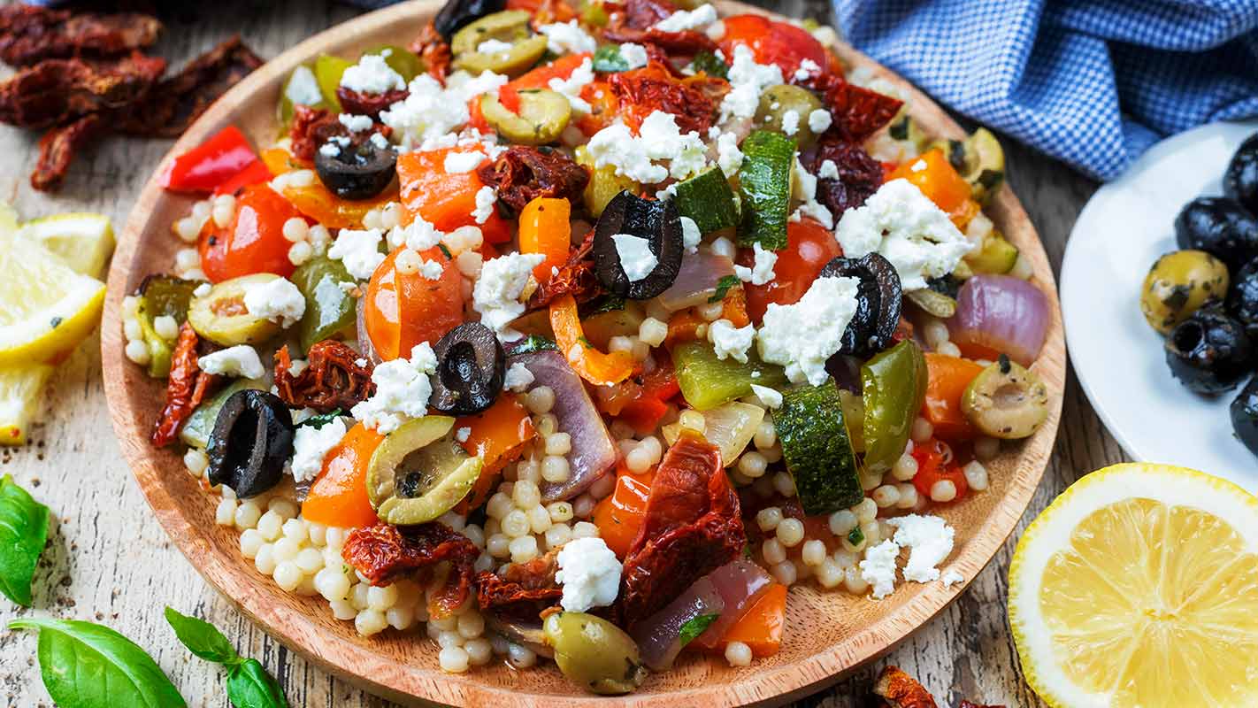 Roasted vegetable couscous salad on a round wooden plate.