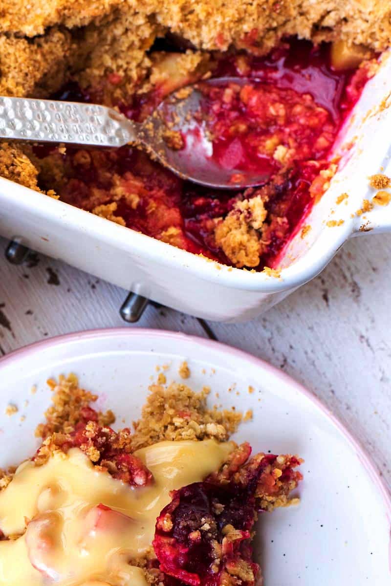 A baking dish of fruit crumble with some spooned out onto a plate.
