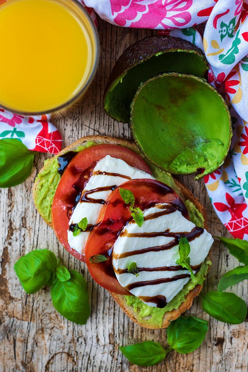 Smashed avocado on toast topped with sliced tomatoes, slices of mozzarella and balsamic vinegar.