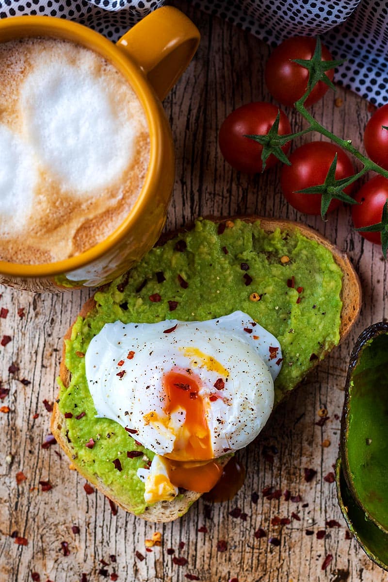 Mashed avocado on toast topped with a poached egg, the yolk spilling out.