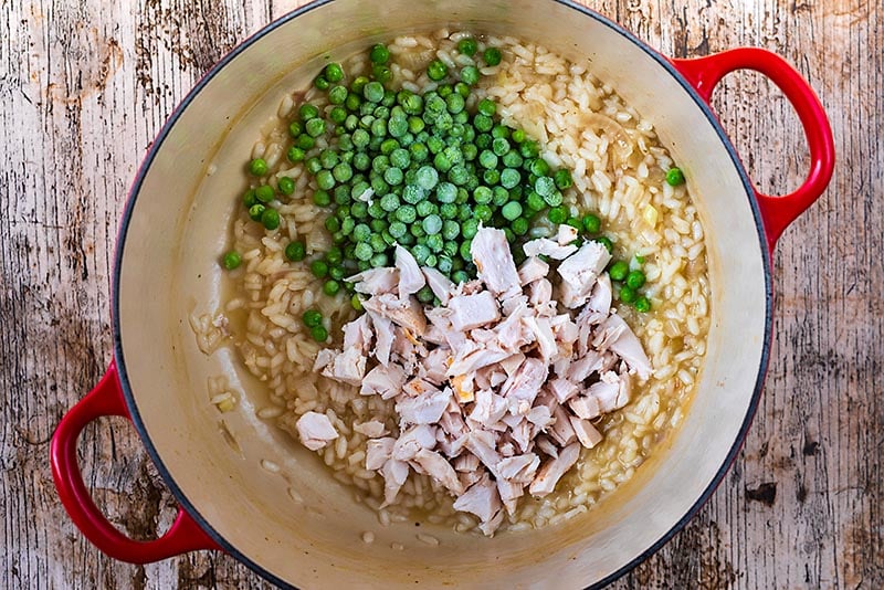 A large red cooking pot containing cooked risotto, chopped chicken and peas.