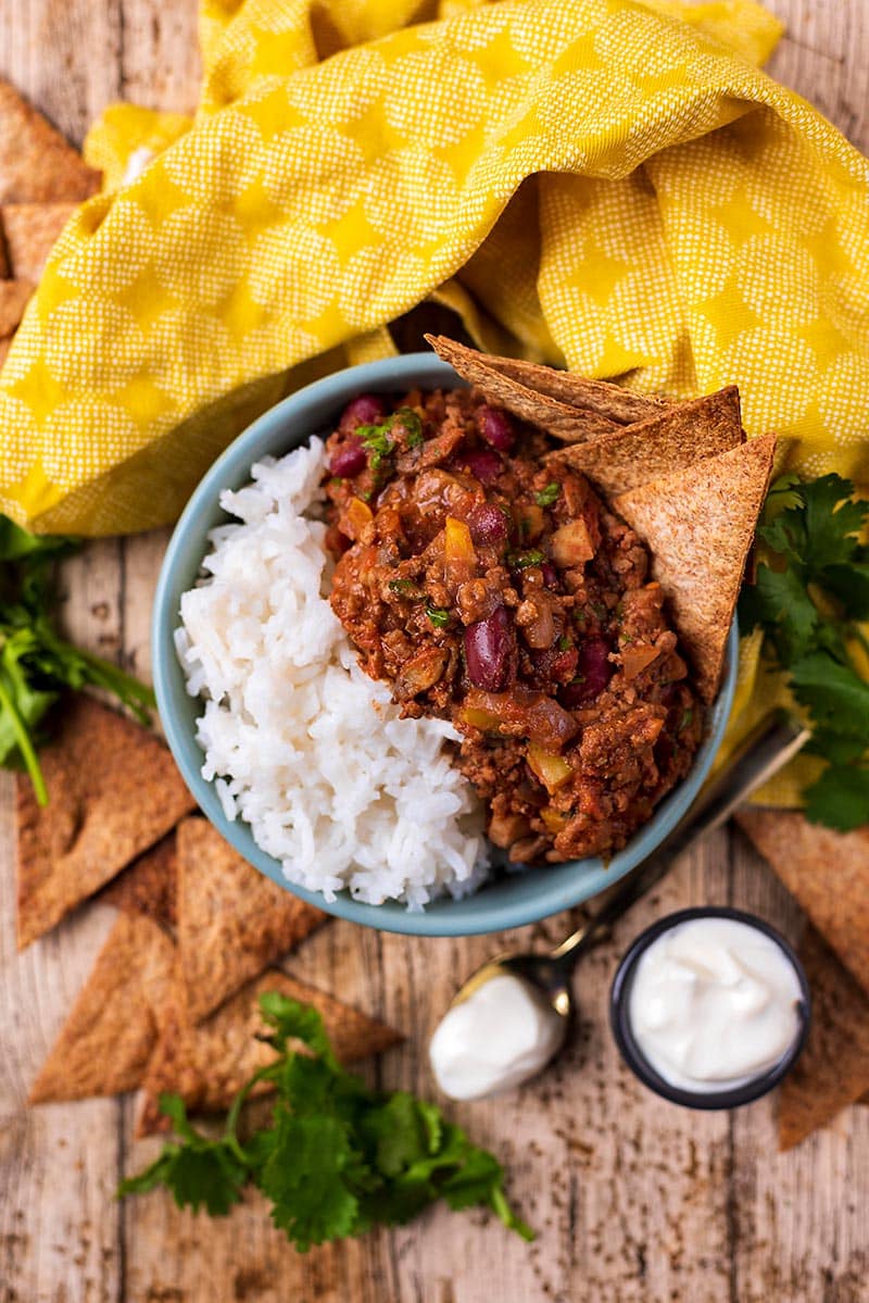 A bowl of chilli con carne and rice with tortilla chips sticking out of the chilli