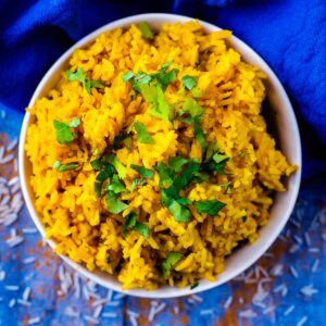 A blue bowl full of turmeric rice topped with chopped herbs.