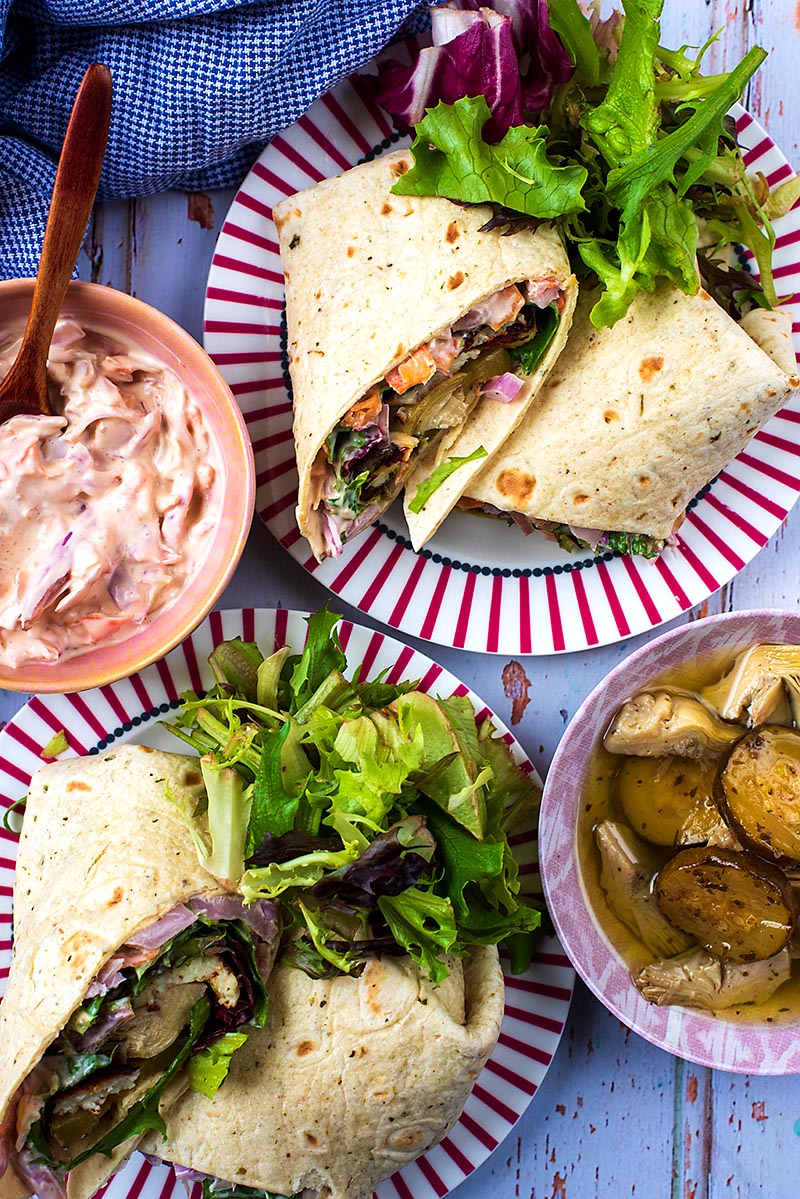 Two Halloumi Wraps on plates with salad, coleslaw and antipasti