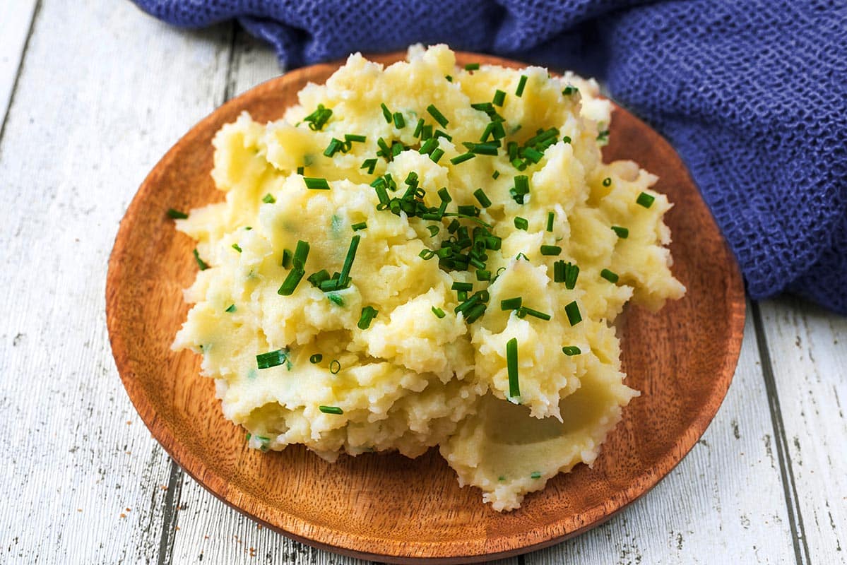A wooden plate with a large serving of Instant Pot Mashed Potatoes.