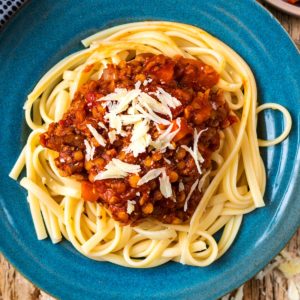 Pasta and lentil bolognese on a blue plate with cheese.