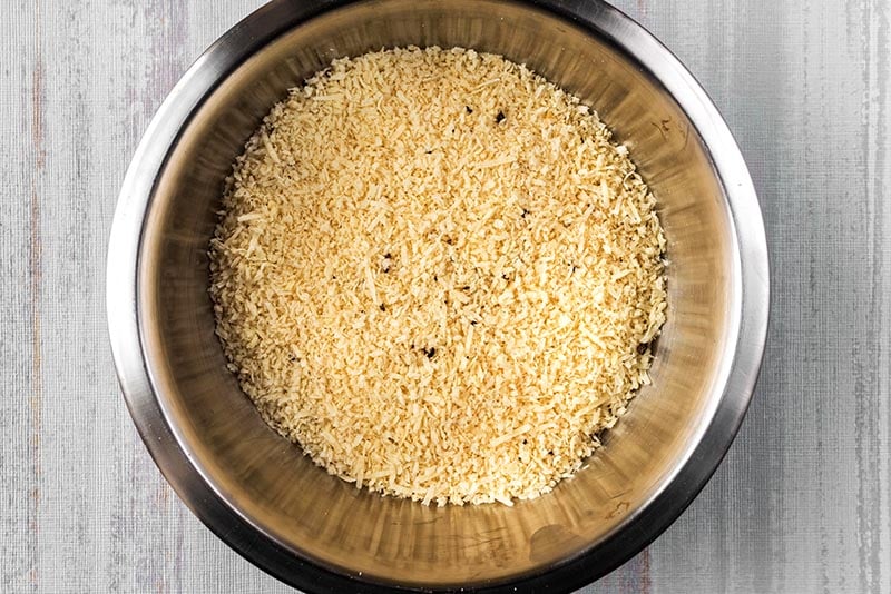 A mixing bowl full of breadcrumbs, grated Parmesan and seasoning.